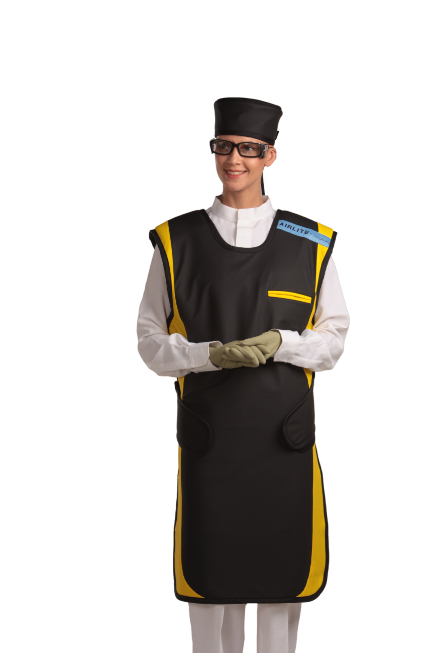 Full frontal view of a female model, her hands clasped together below her chest, wearing a radiation protection head shield, eyewear, medical gloves, and a coat apron with closed velcro fasteners by the sides. The apron is jet-black with yellow-colored lines by the edges.  