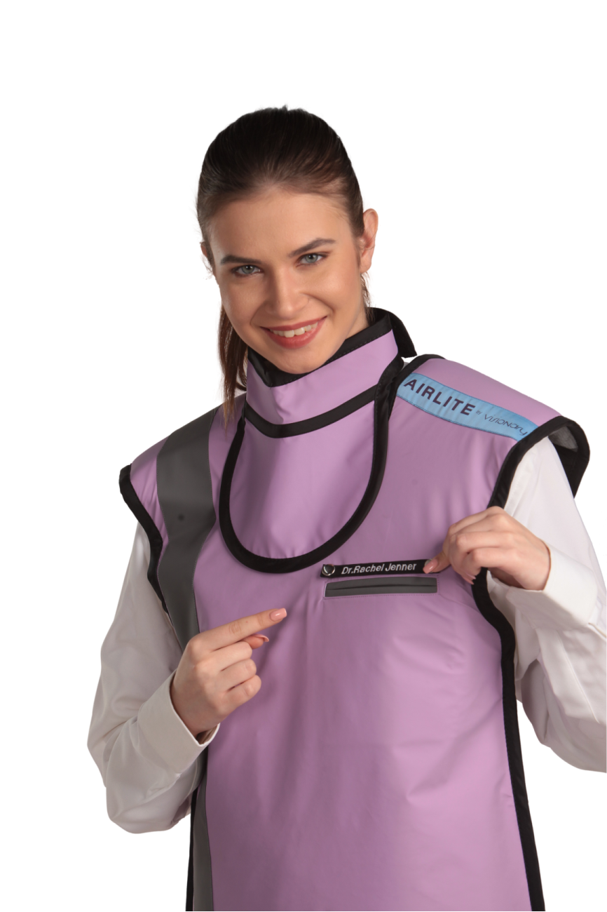 A female model wearing a lilac coat apron with integrated thyroid guard. She is pointing to an inscribed doctor's tag on the apron.