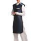 A partial frontal view of a female model wearing a navy blue, beige-lined coat apron with flex back. Her hands are clasped below her chest 