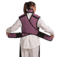 Back view of a female model wearing a coat apron with a flex back and an integrated thyroid guard. The apron is mauve in color with a Jet black center line and has unfastened velcro fasteners by the sides held in the model's hands.